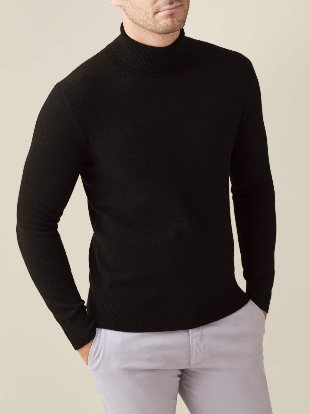 Front view of a model wearing a black cashmere roll neck jumper paired with light grey trousers.