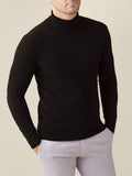Front view of a model wearing a black cashmere roll neck jumper paired with light grey trousers.