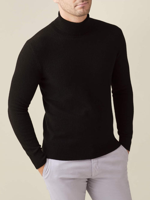 Front view of a model wearing a black cashmere roll neck jumper paired with light grey trousers.