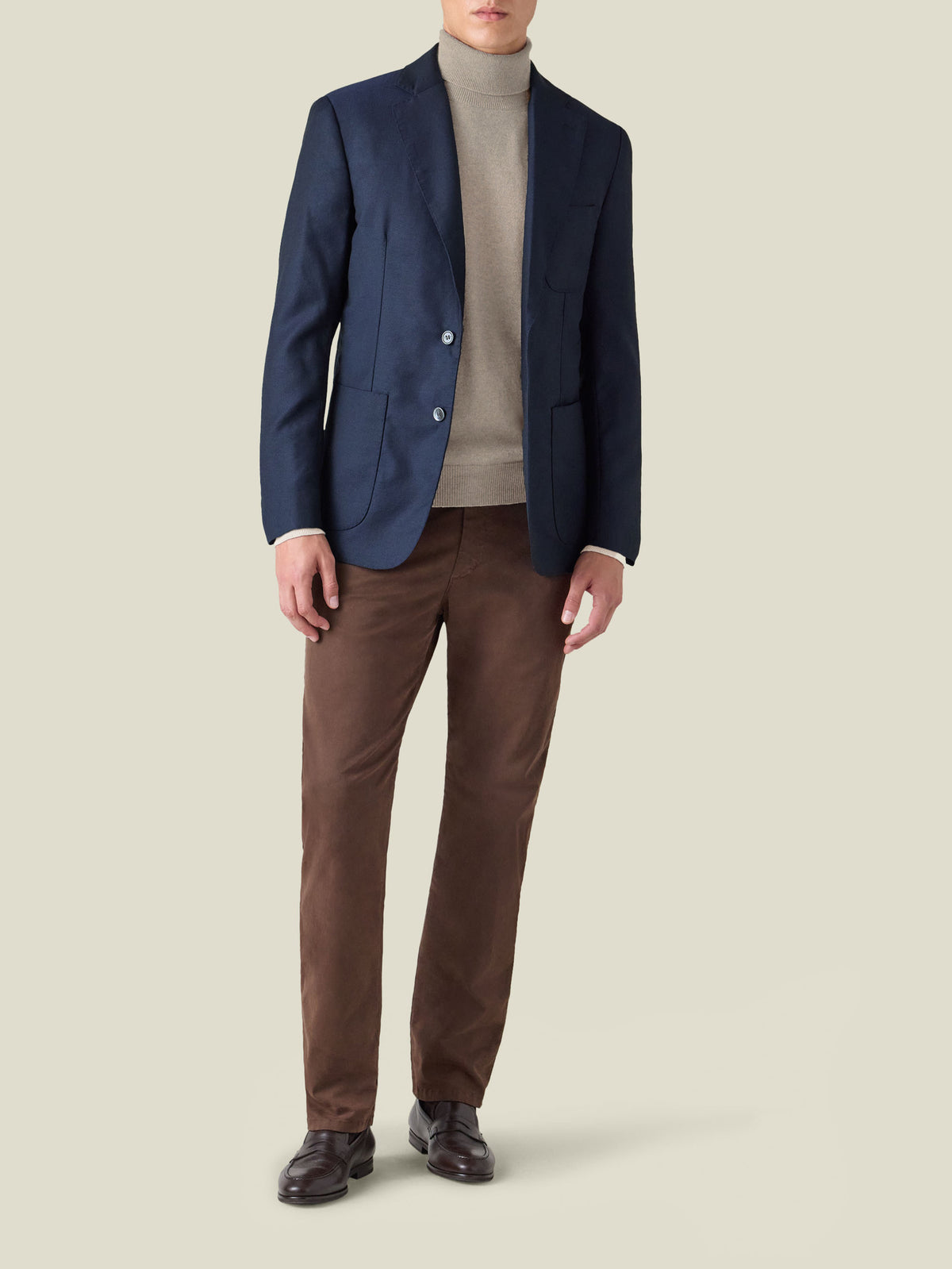 Front view of a model wearing the Luca Faloni Almond Cashmere Roll Neck with a navy blazer and brown trousers.