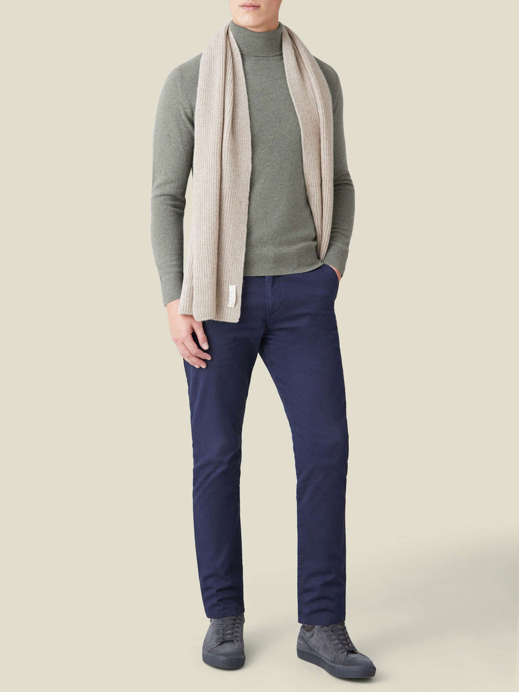 Model wears Luca Faloni's moss green cashmere roll neck with a beige scarf and navy trousers.