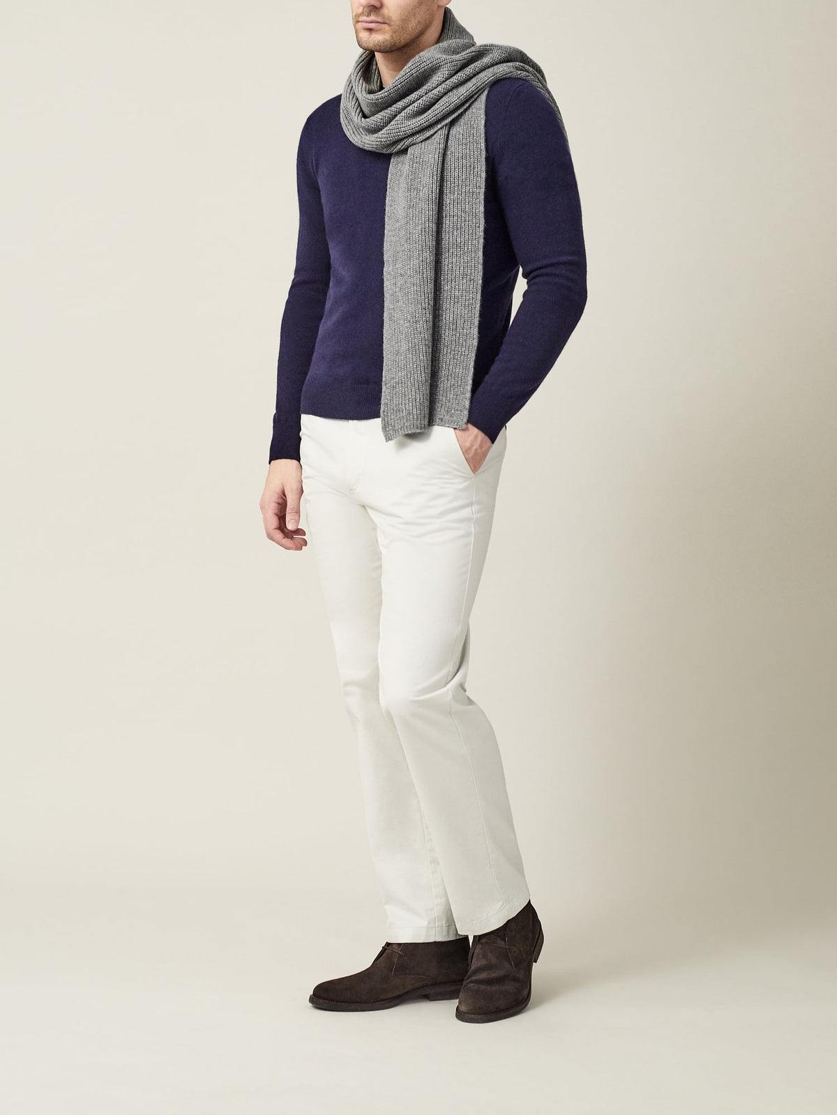 A man wears the Dolomiti Grey Chunky Knit Cashmere Scarf, styled with a navy blue knit, white trousers, and brown shoes.