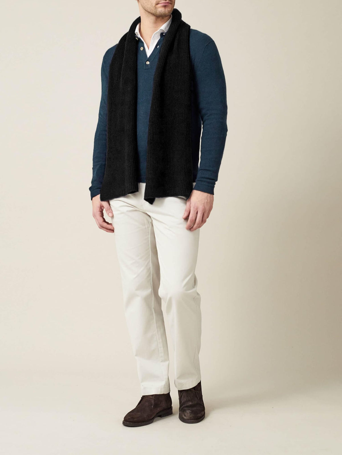 A model wears the black Chunky Knit Scarf from Luca Faloni, paired with a blue sweater and white trousers.