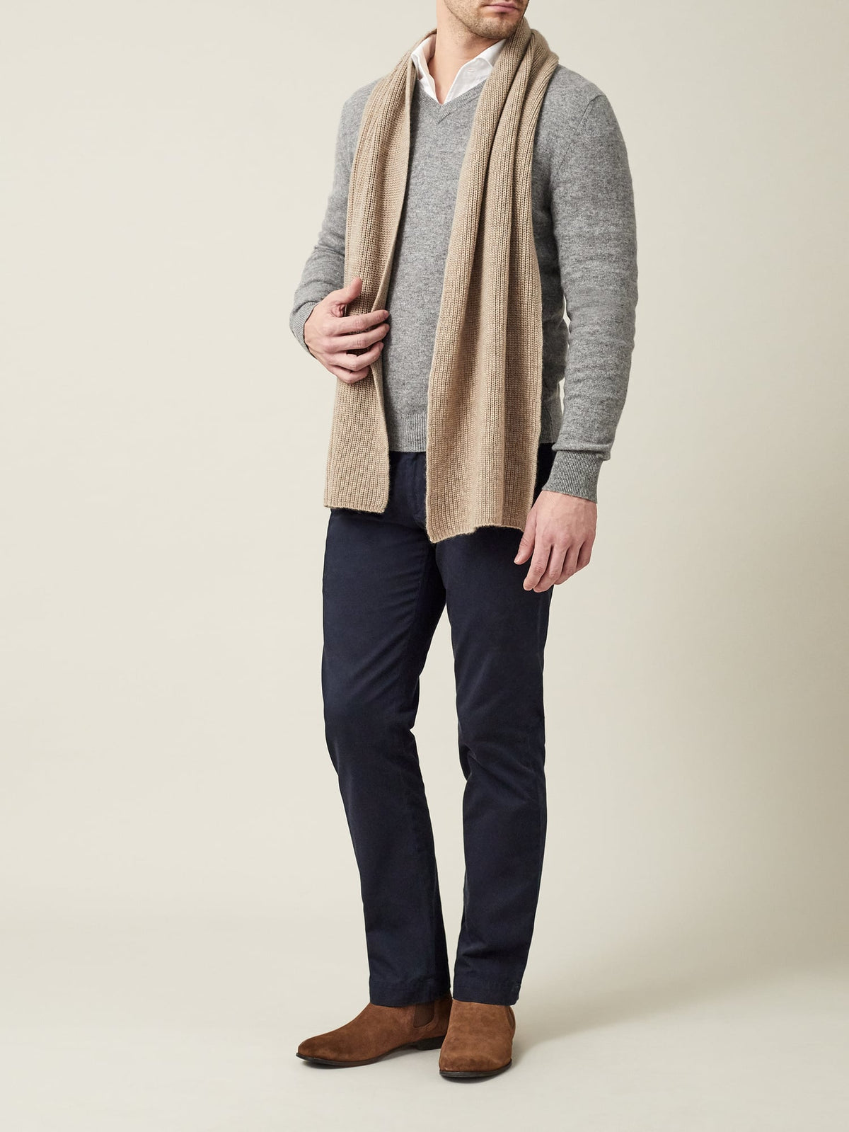 A model styles the camel beige chunky knit cashmere scarf over a grey sweater, paired with navy trousers and brown boots.