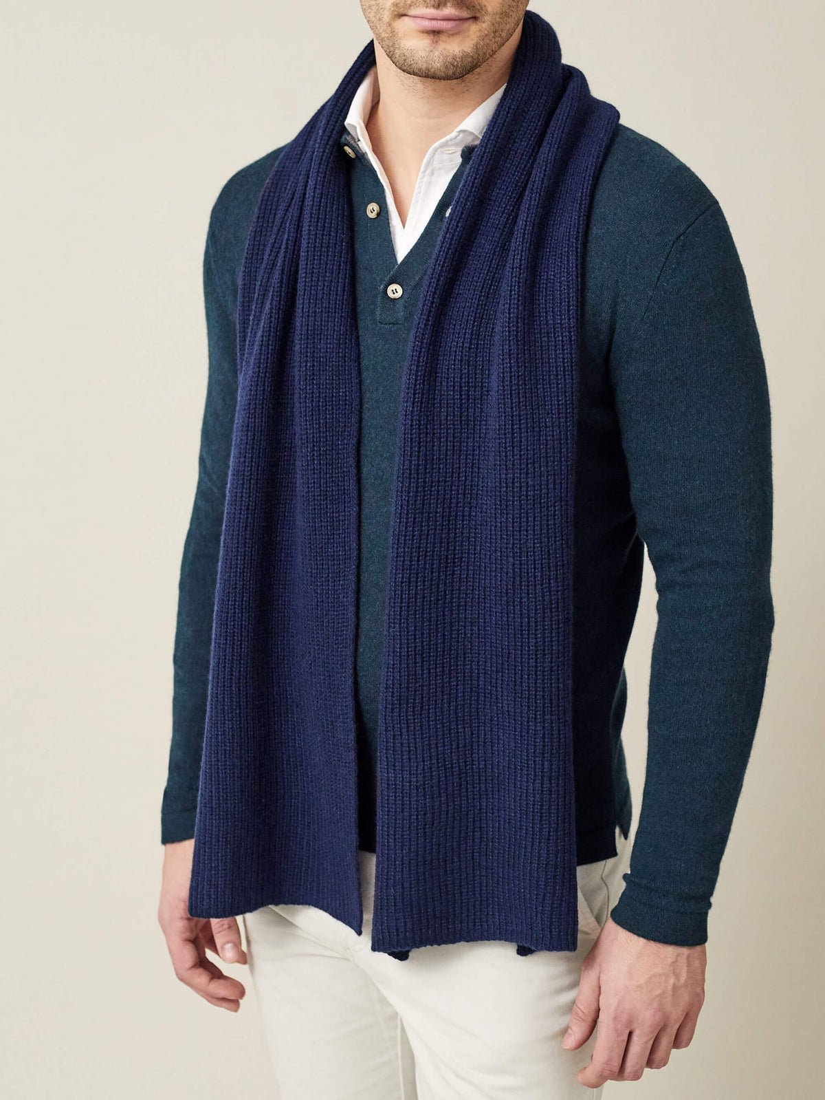 A man models the Luca Faloni Chunky Knit Cashmere Scarf in midnight blue, worn over a teal polo and white trousers.