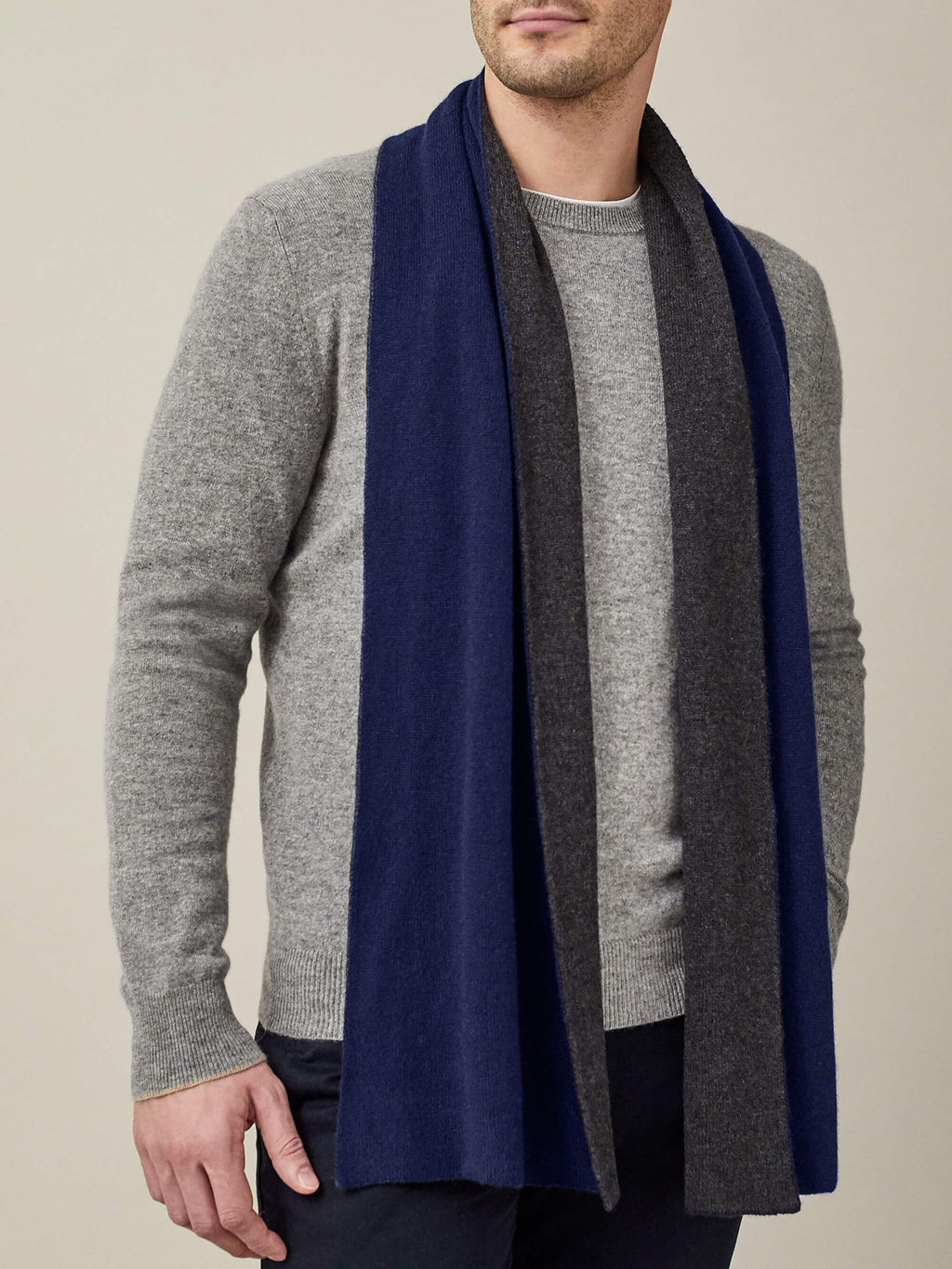 A man wearing the Luca Faloni Double-Faced Cashmere Scarf in Navy and Charcoal over a light grey sweater.