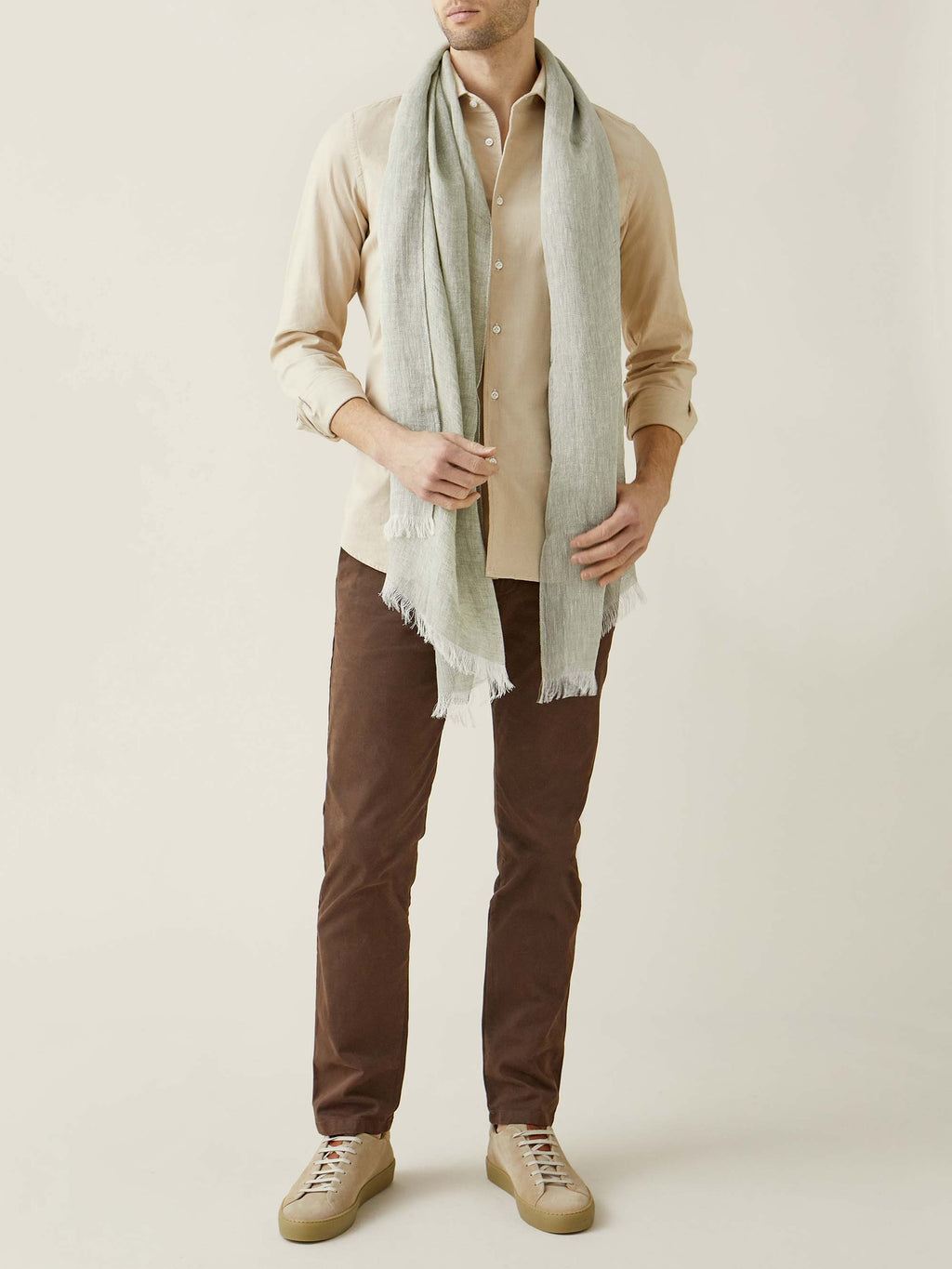 A full-length shot of a model wearing the Luca Faloni Khaki Green Linen Scarf, styled with a sand shirt and brown trousers.