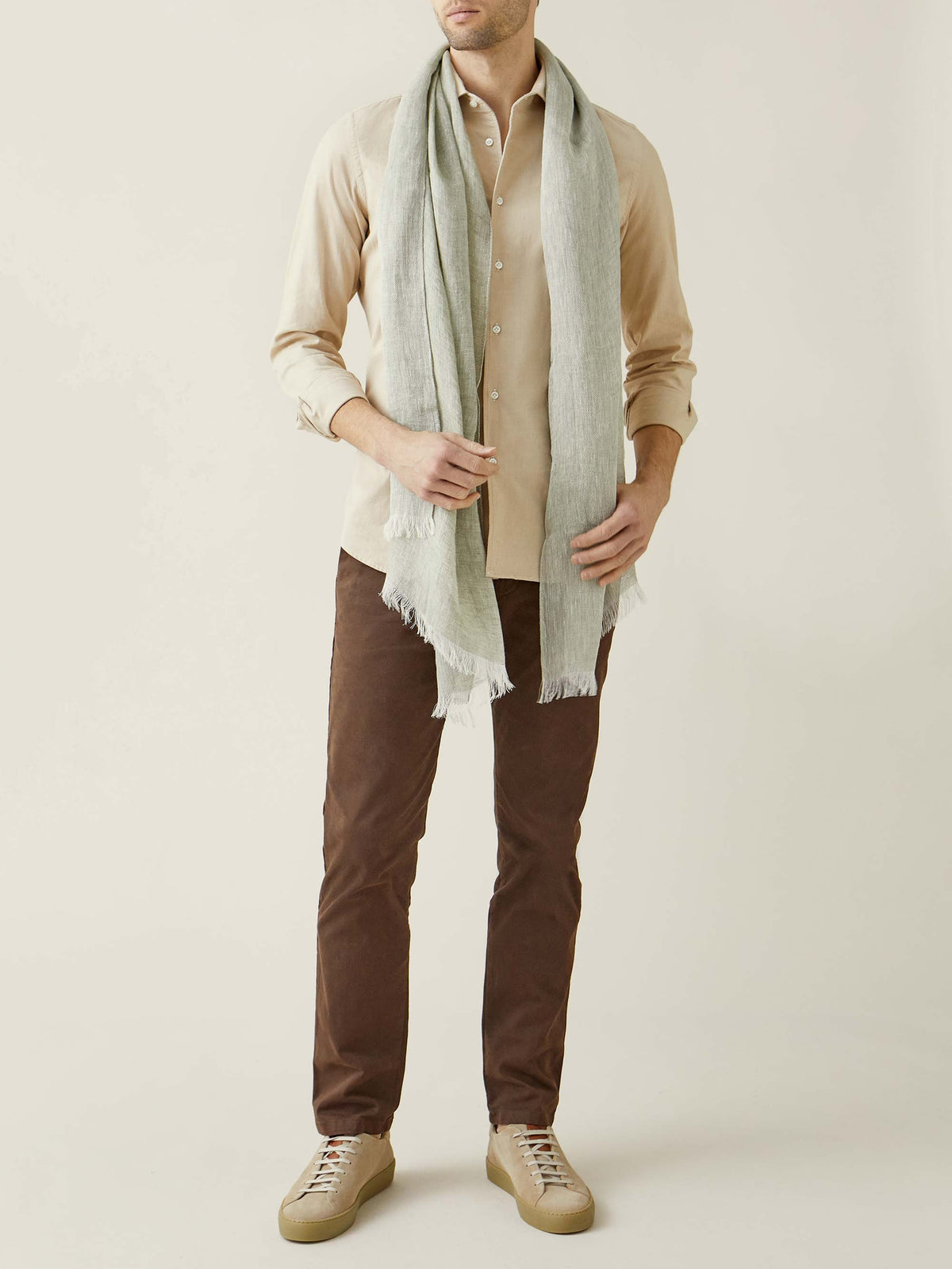 A full-length shot of a model wearing the Luca Faloni Khaki Green Linen Scarf, styled with a sand shirt and brown trousers.