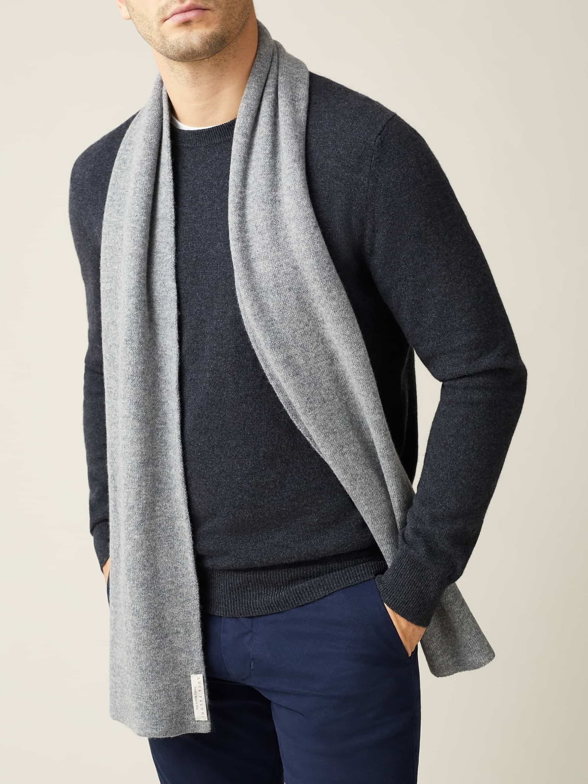 A man models the Luca Faloni Cashmere Scarf in Dolomiti Grey, worn over a dark grey sweater and navy trousers.