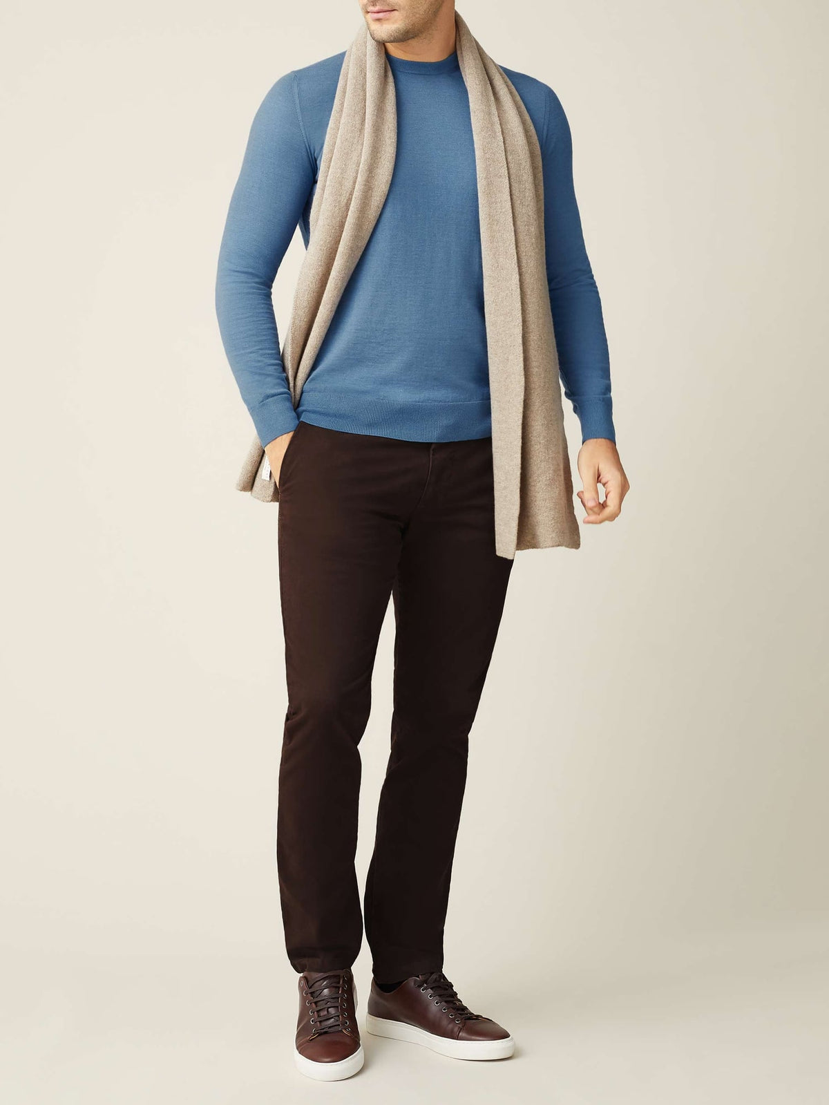 Full-length view of a model wearing the Luca Faloni Camel Beige Cashmere Scarf over a blue sweater and dark brown trousers.