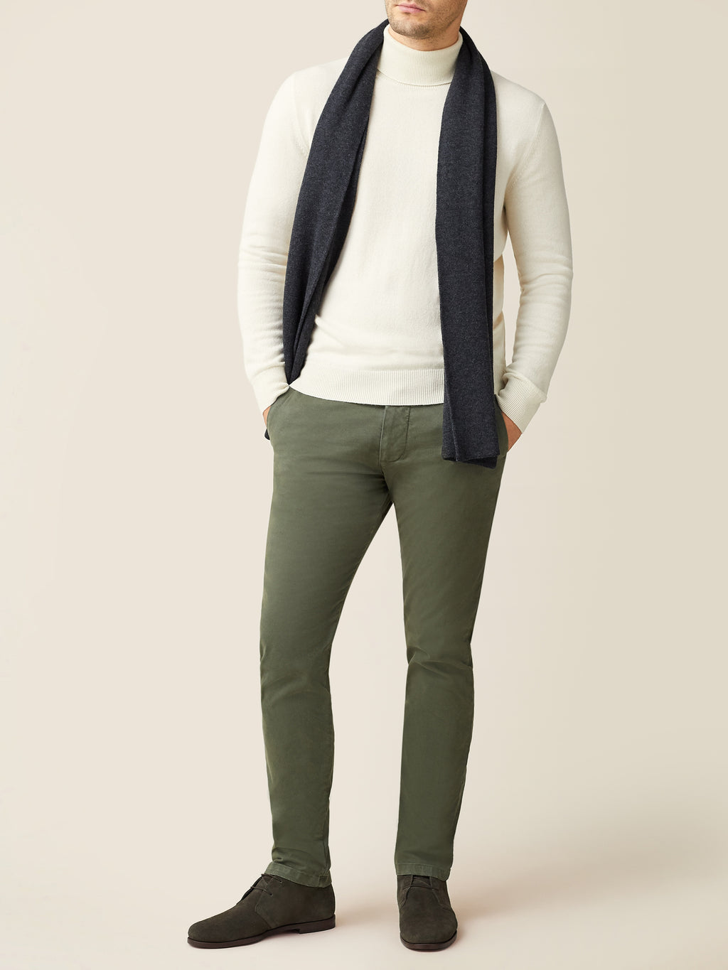 A man models the Luca Faloni charcoal grey cashmere scarf, styled with a cream turtleneck sweater and olive green trousers.