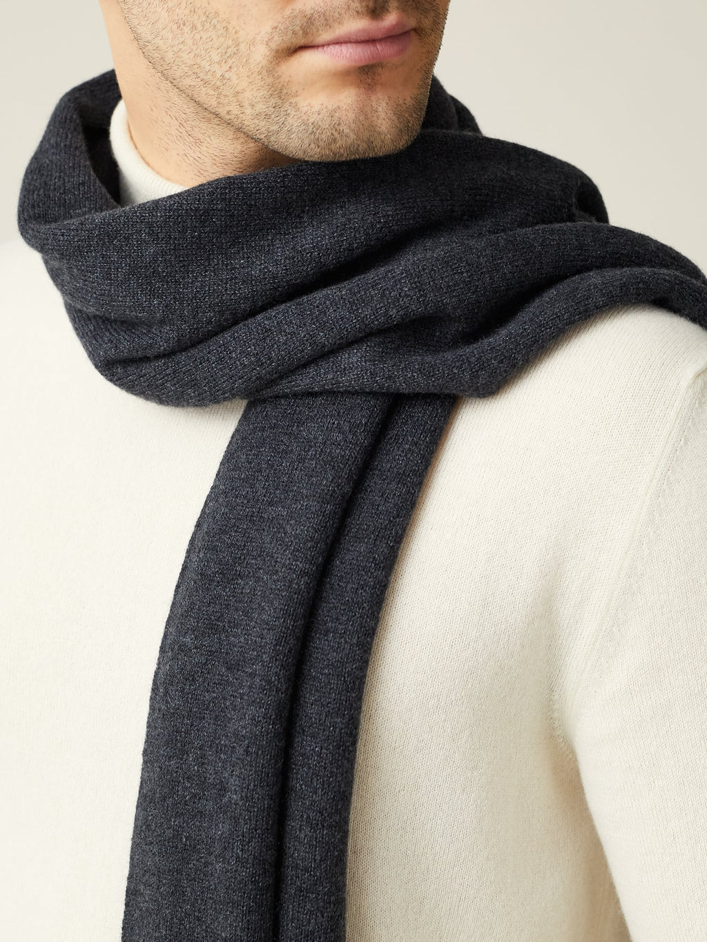 A close-up view of a man wearing the Luca Faloni Charcoal Grey Cashmere Scarf over a cream turtleneck.
