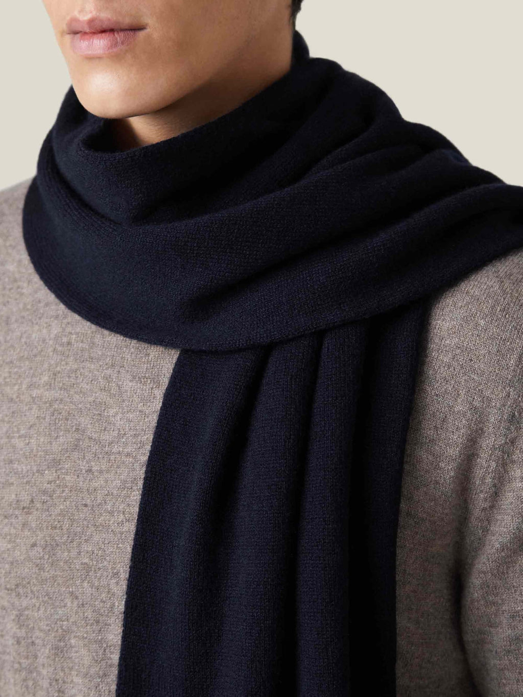 A close-up of a man wearing the Luca Faloni Midnight Blue Cashmere Scarf, styled over a light grey knit sweater.