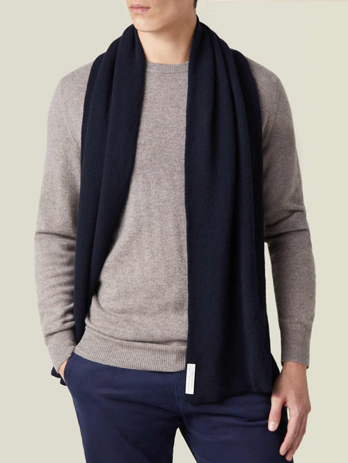 A front view of a model wearing the Luca Faloni Midnight Blue Cashmere Scarf over a light brown sweater and navy trousers.