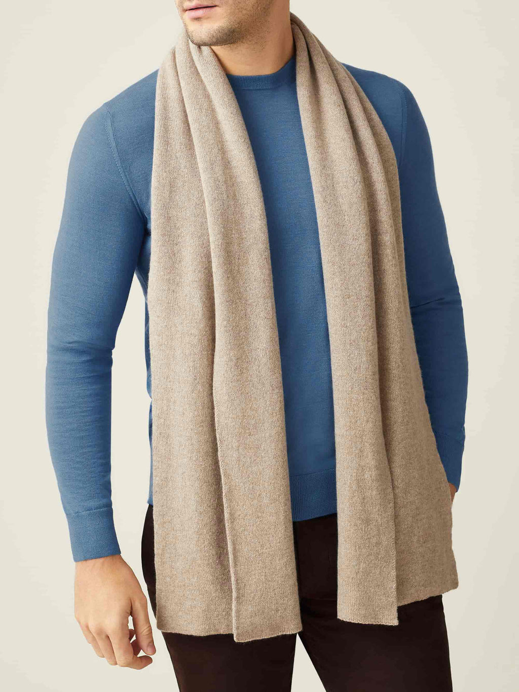 Front view of a model wearing the Luca Faloni Cashmere Scarf in Camel Beige, styled over a blue crewneck sweater.
