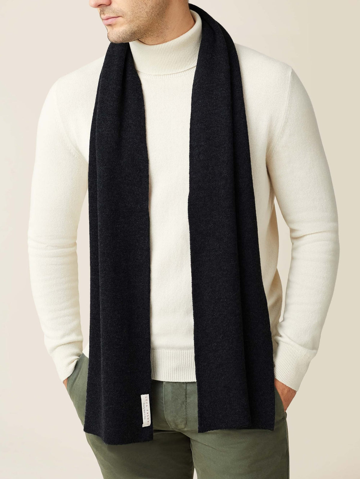 Model wearing the Luca Faloni black cashmere scarf over a cream turtleneck and olive green trousers.