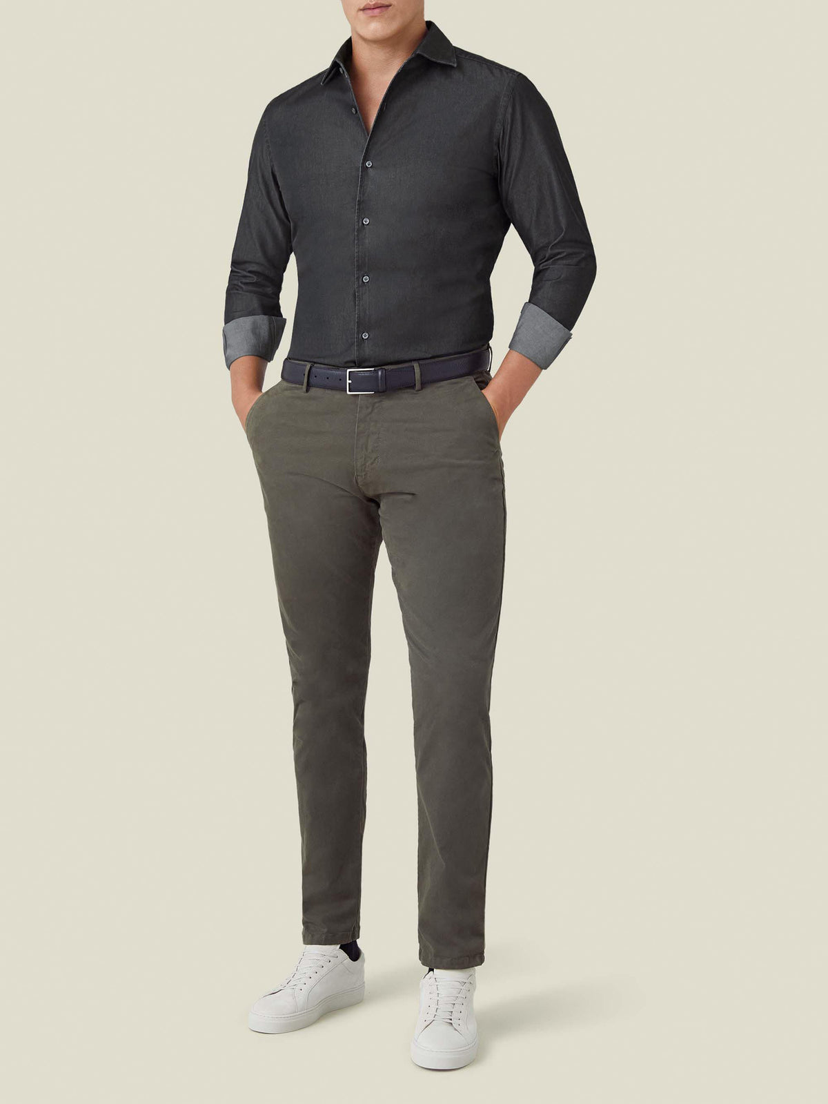 Model wears a black Denim Shirt with olive chinos and white sneakers. Full-body view against a studio background.