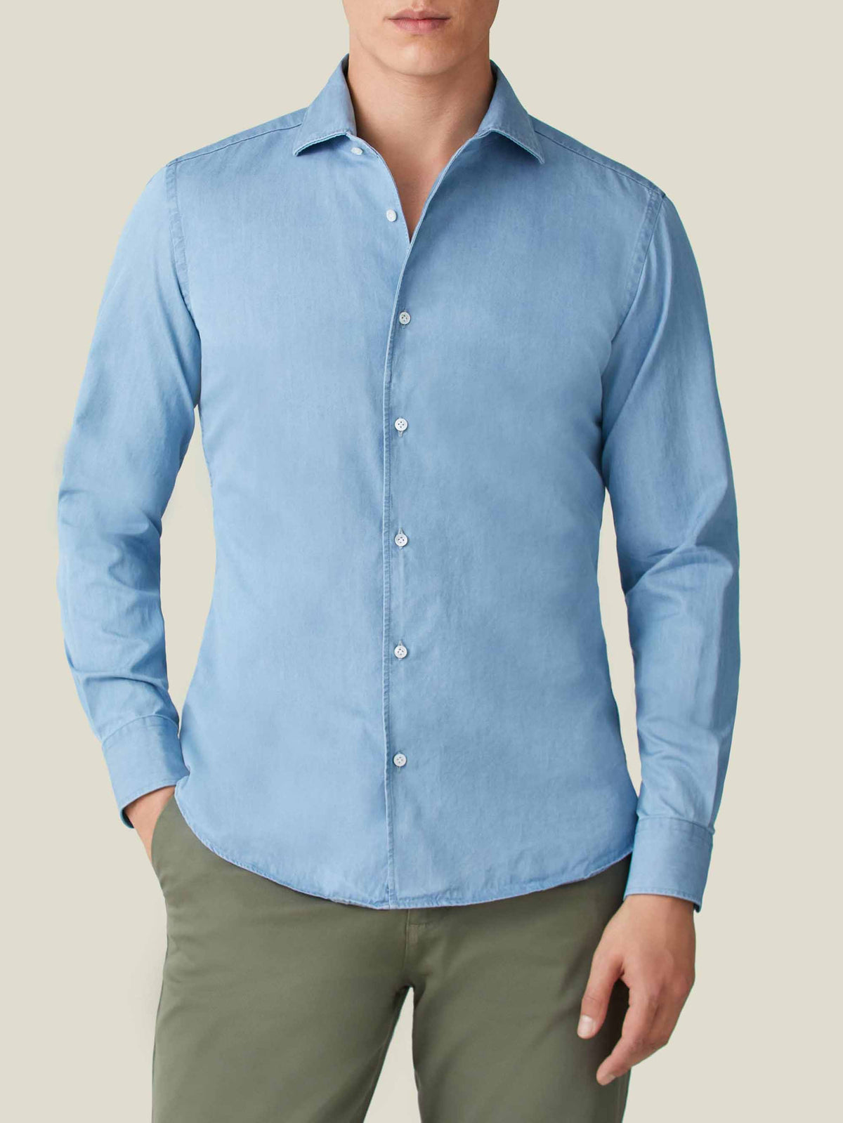 A man models the Luca Faloni light blue denim shirt, paired with olive green chinos.