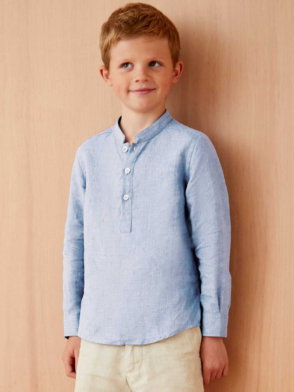 A boy wears the Forte Junior Linen Shirt in sky blue, featuring a band collar and long sleeves, against a plain backdrop.