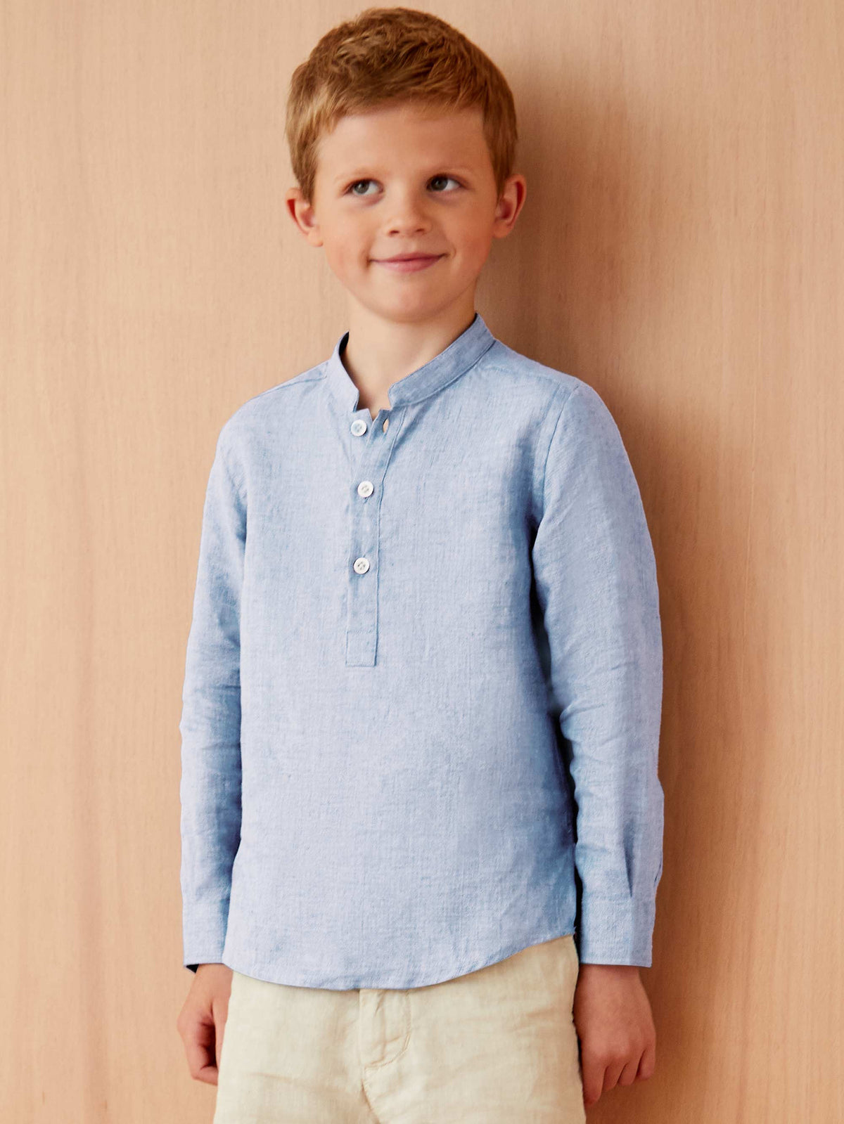 A boy wears the Forte Junior Linen Shirt in sky blue, featuring a band collar and long sleeves, against a plain backdrop.