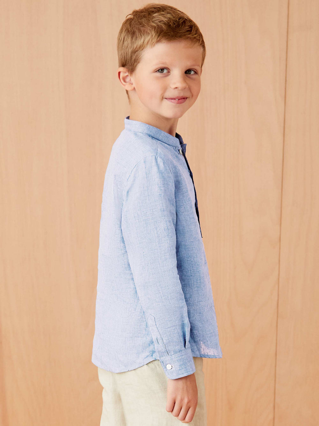 Side profile of a young boy wearing the sky blue Forte Junior Linen Shirt, highlighting the band collar and fit.