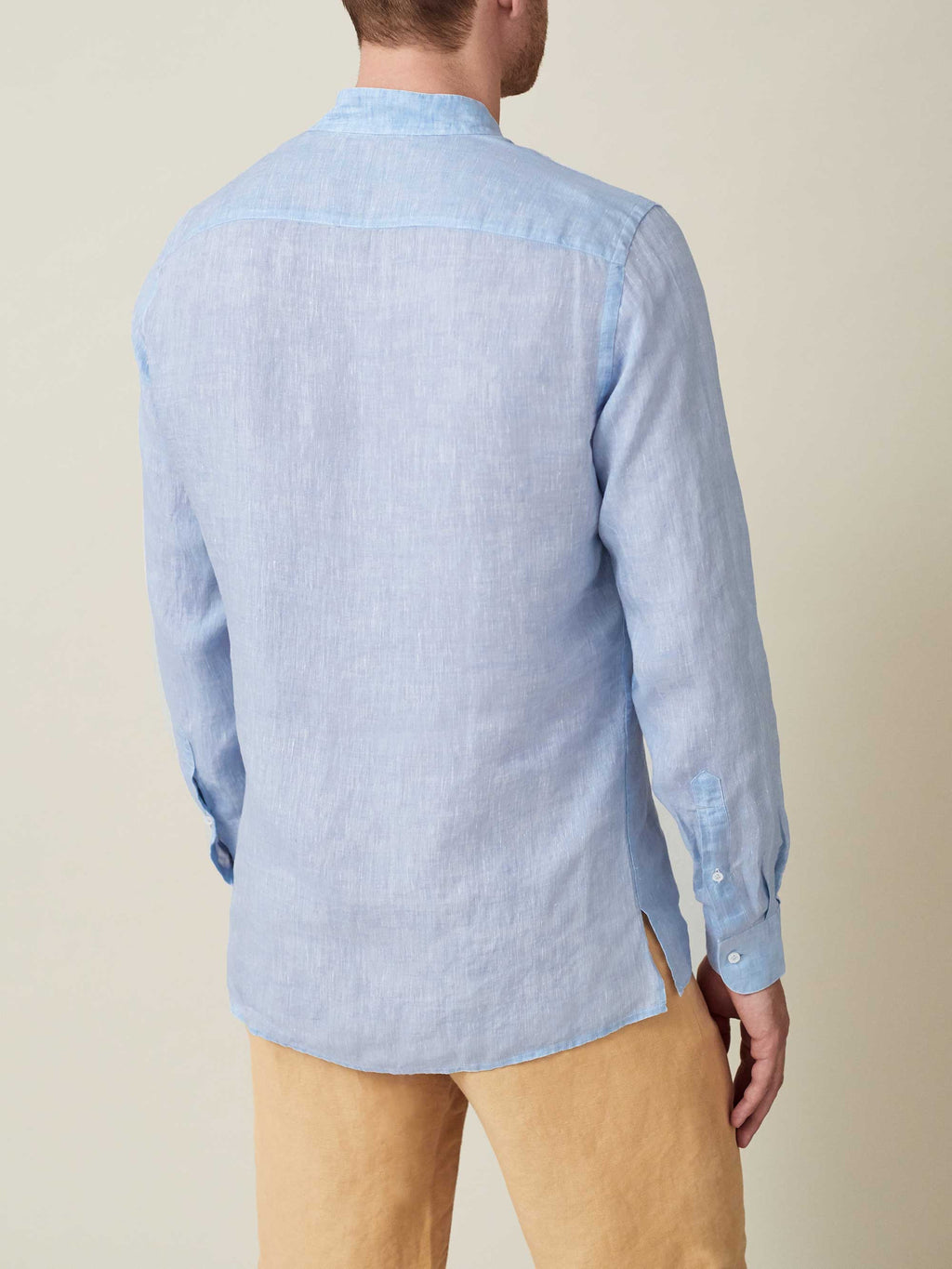 Model from the back wearing the sky blue Forte Linen Shirt, showing the band collar and softly curved split hem.