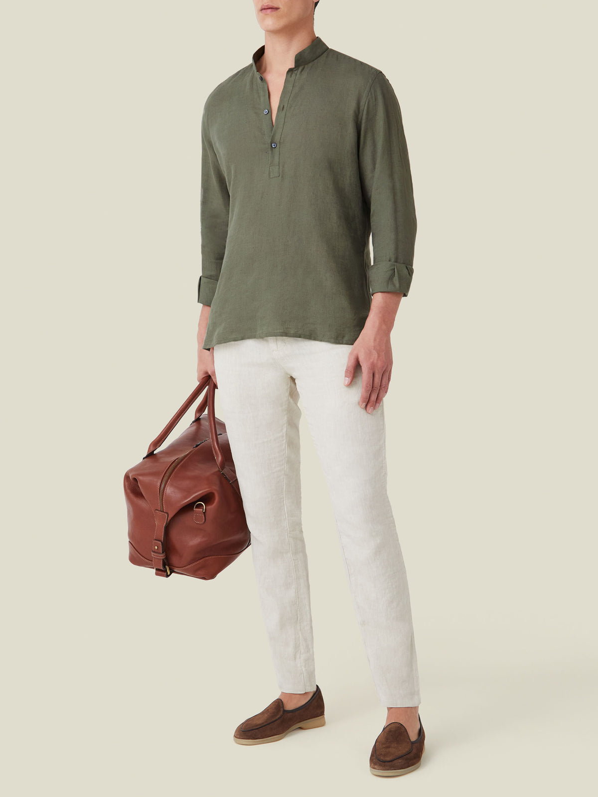 A model wears the Khaki Green Forte Linen Shirt with white linen trousers, brown suede loafers, and a leather weekender bag.