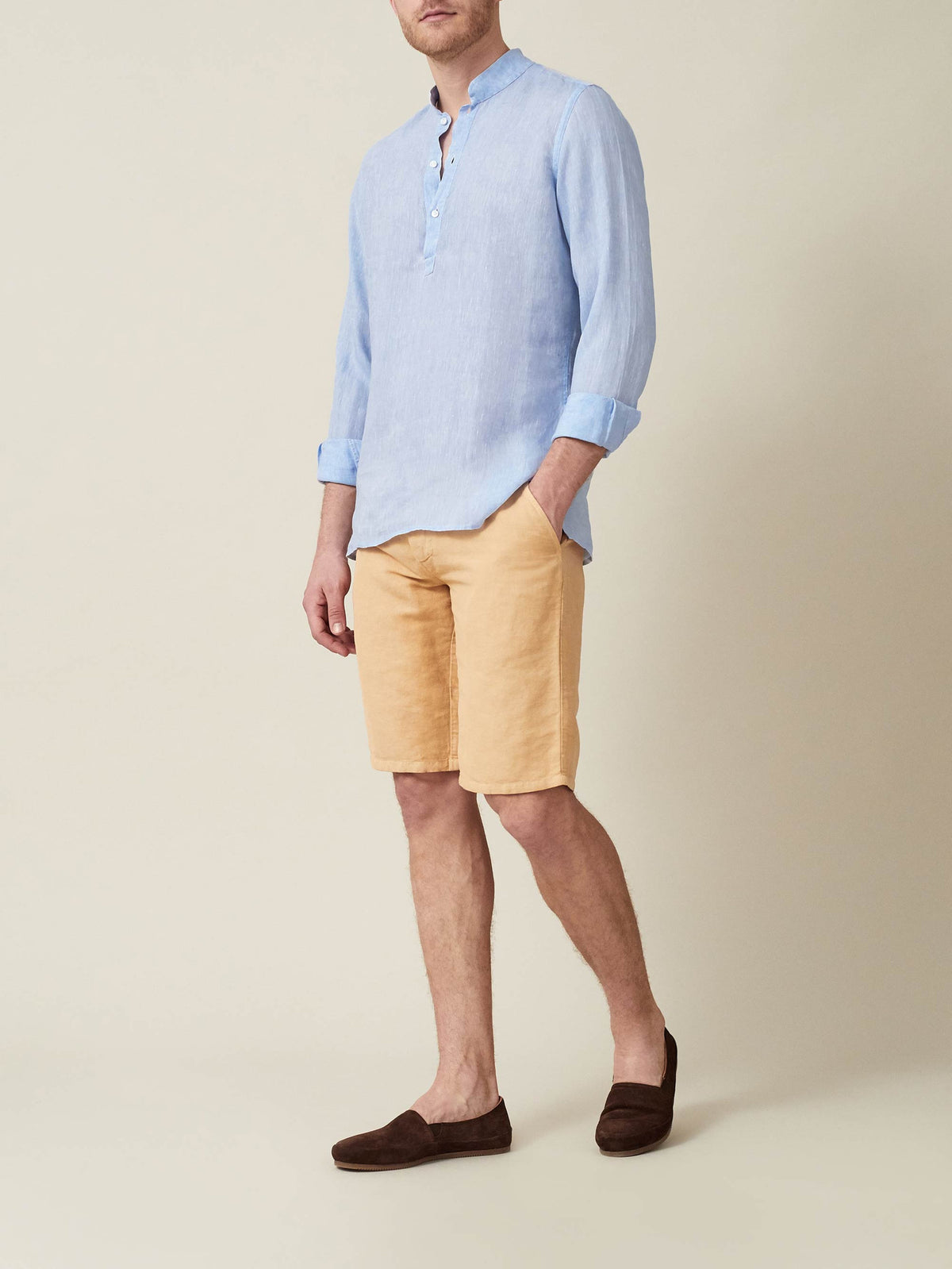 Man wearing sky blue Forte Linen Shirt with band collar and rolled-up sleeves, paired with yellow shorts and brown loafers.