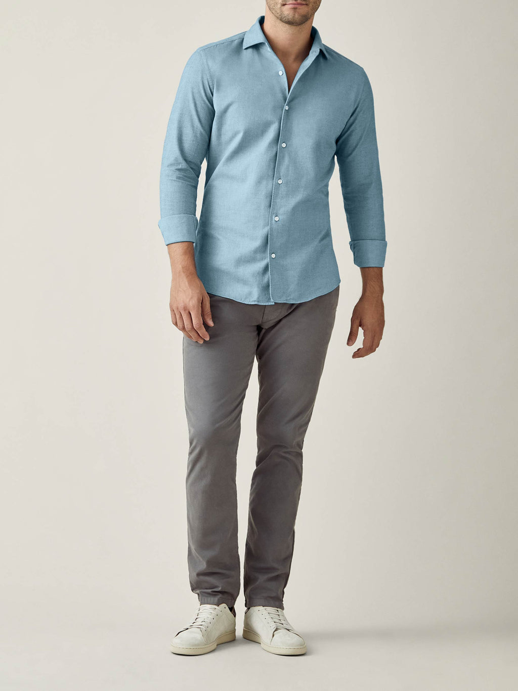 Man wearing the Brushed Cotton Shirt in Topaz, styled with grey trousers and white sneakers, against a studio backdrop.