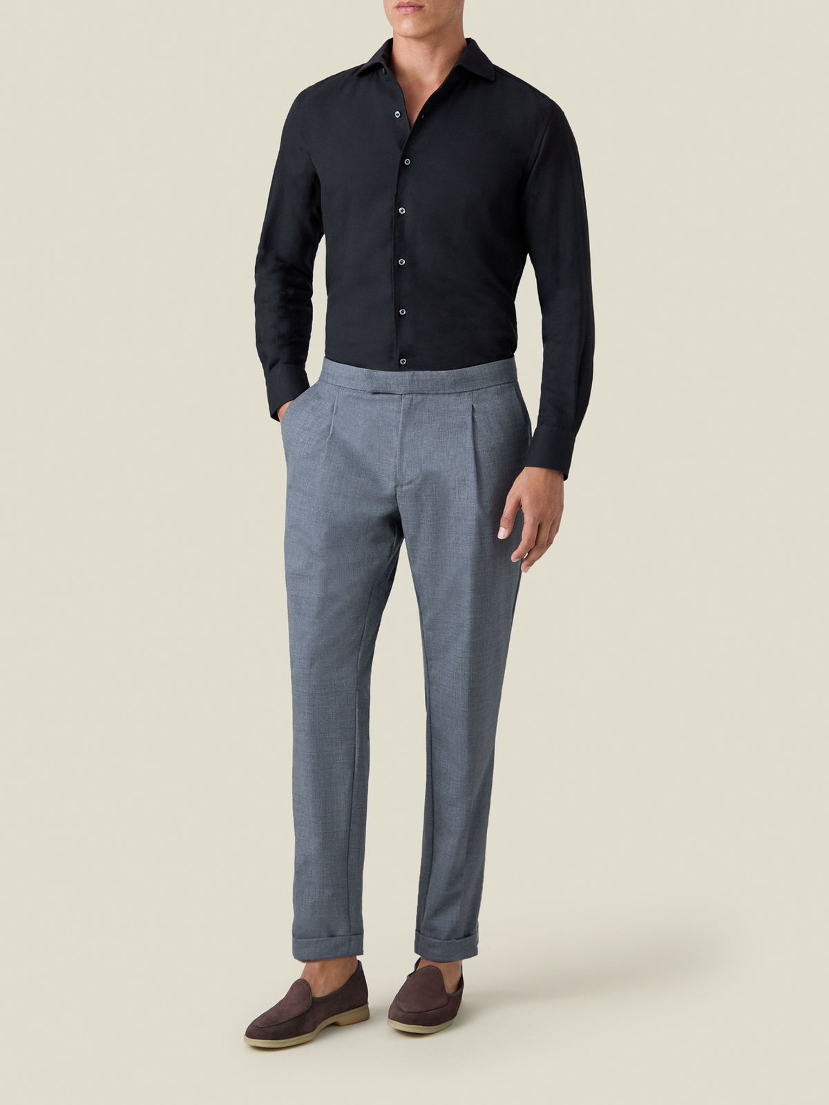 Model wears the Luca Faloni black Cashmere-Cotton Shirt with grey-blue pleated trousers and brown loafers.