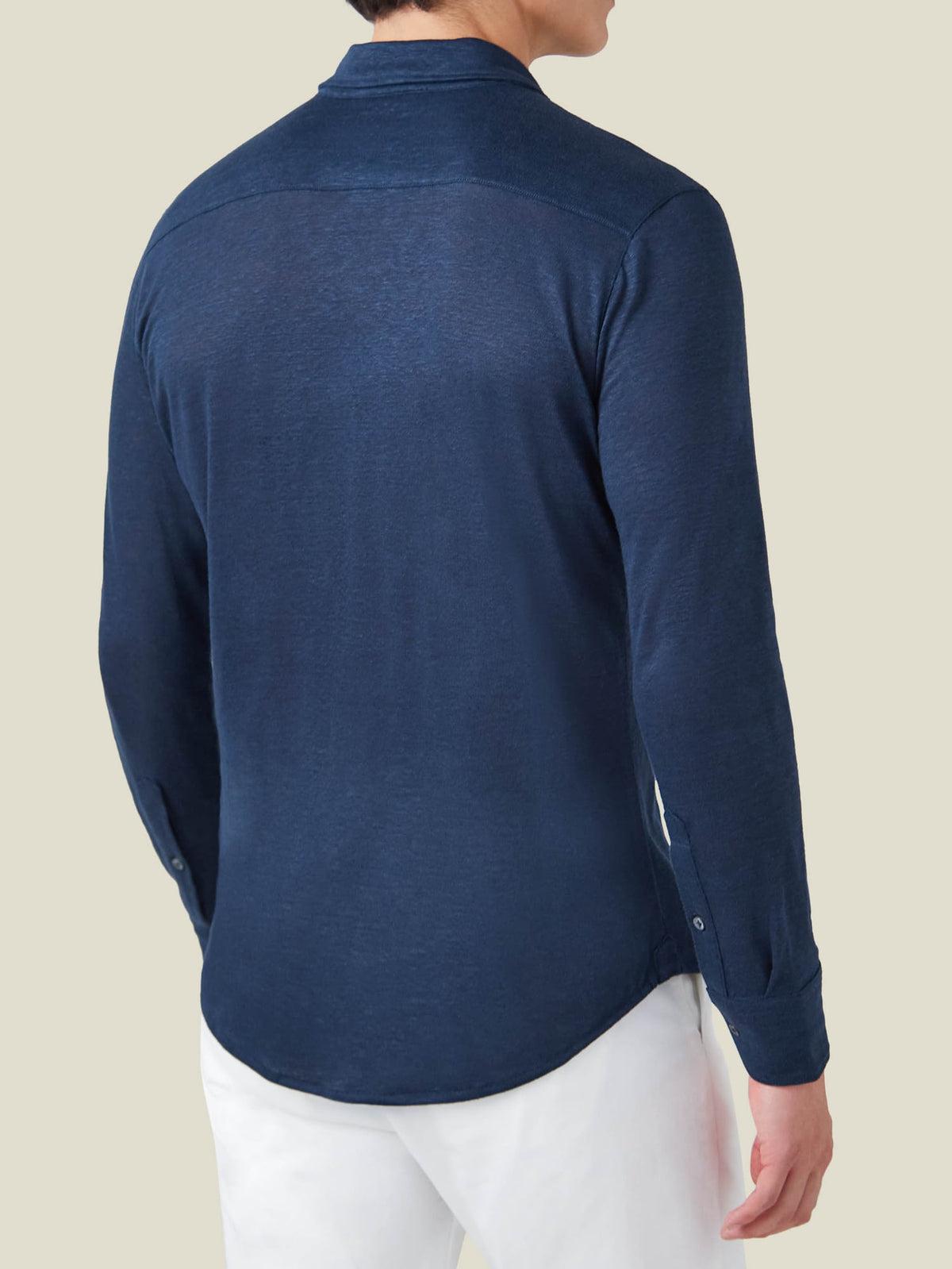 Back view of a man wearing the Linen Jersey Shirt in navy blue, paired with white trousers.