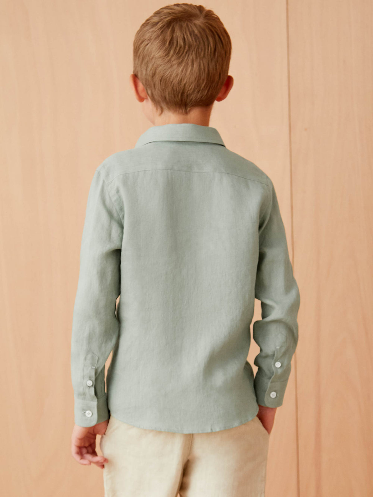 Back view of a boy wearing the Portofino Junior Linen Shirt in sage green.