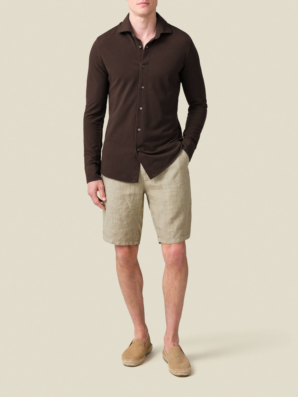 A model wears the Siena Piqué Shirt in Chocolate Brown, styled with beige linen shorts and matching espadrilles.