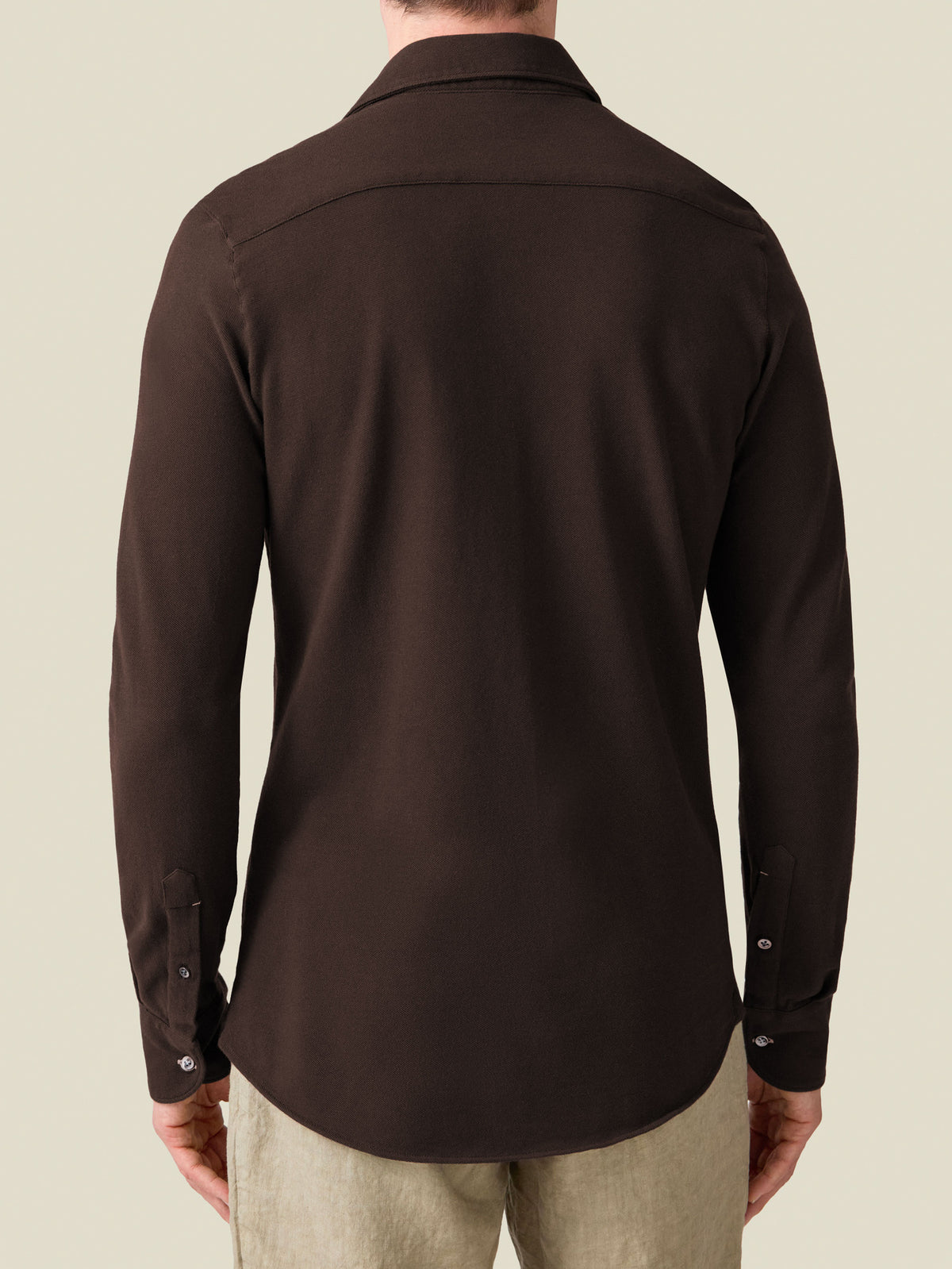 Model wears the Siena Piqué Shirt in Chocolate Brown, pictured from the back to showcase the fit and rounded hemline.