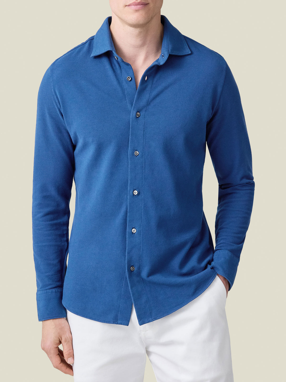 A model wears the Siena Piqué Shirt in Royal Blue with white trousers in a front-facing studio shot.