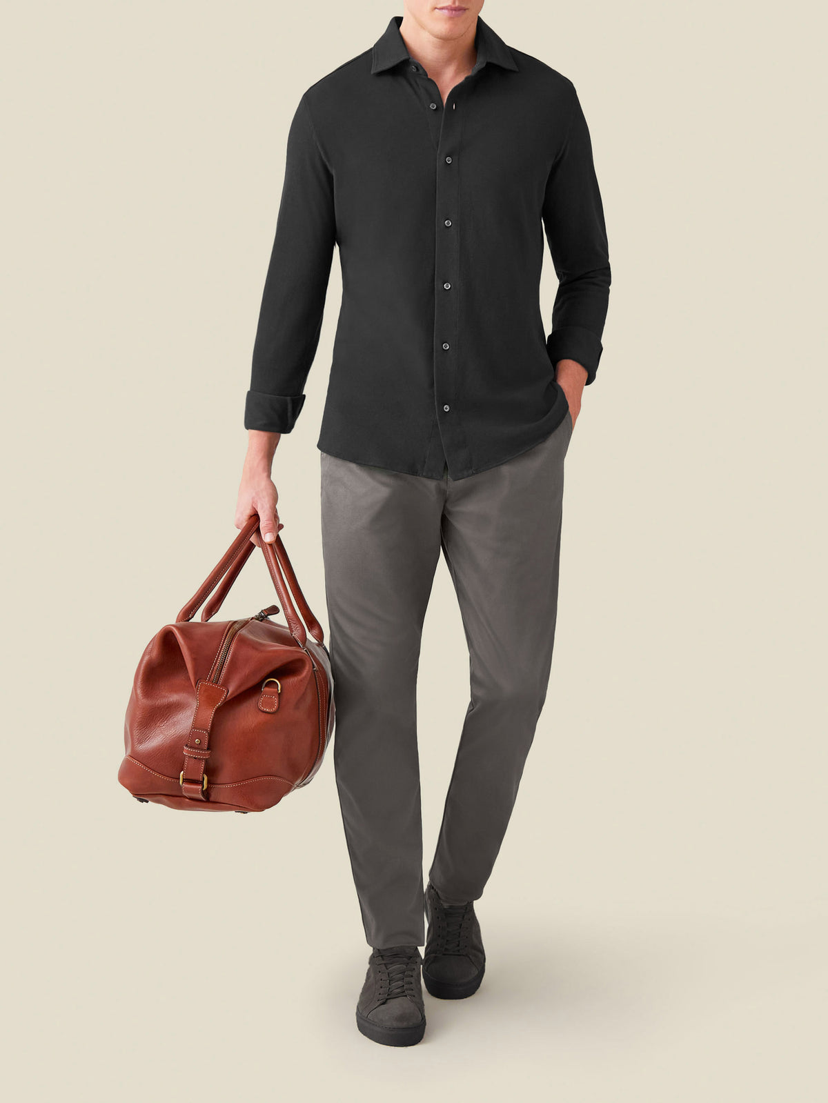 Model wearing the Siena Piqué Shirt in Charcoal Grey, paired with grey trousers and carrying a brown leather travel bag.