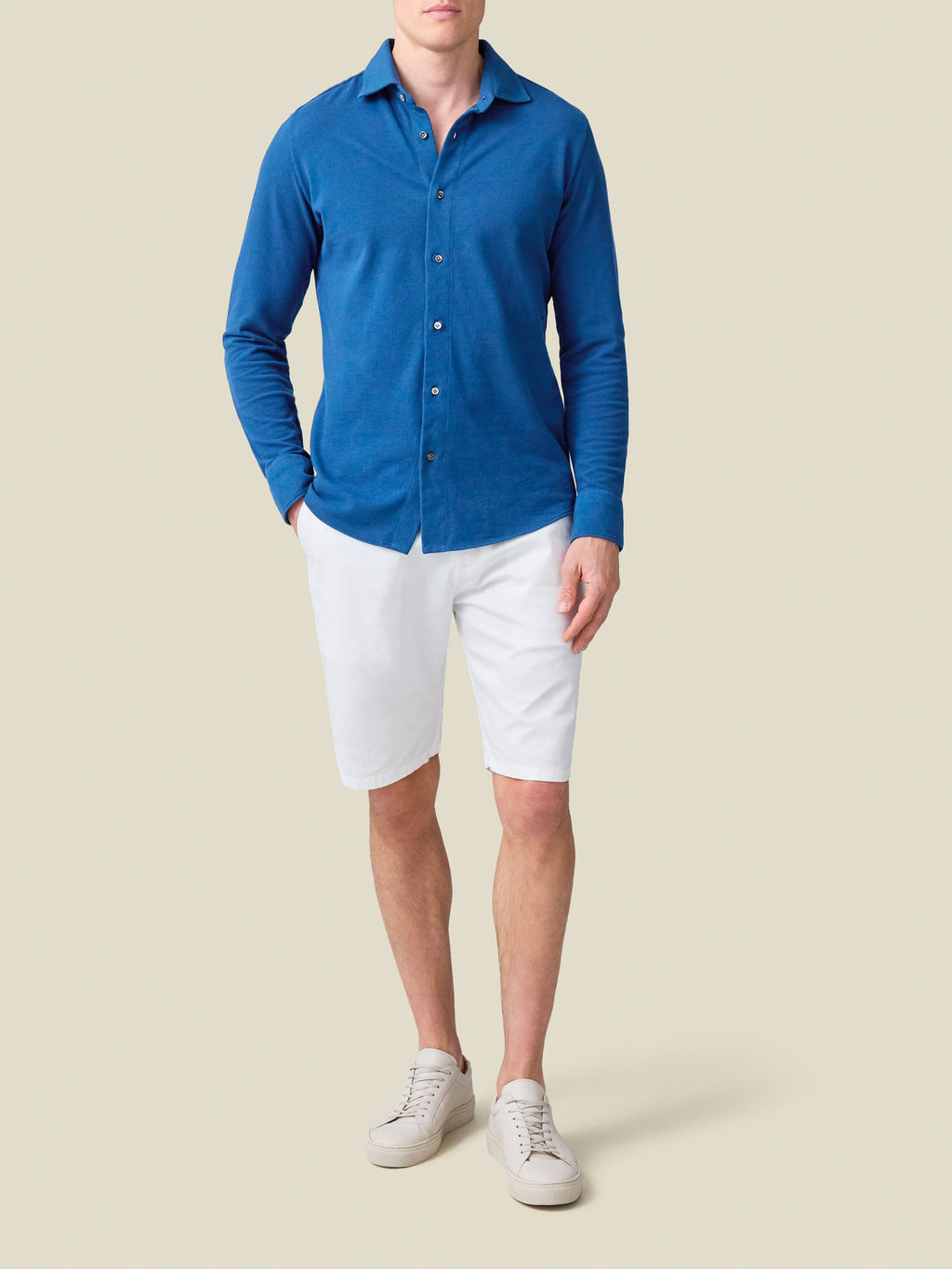 Full-length shot of a model wearing the royal blue Siena Piqué Shirt by Luca Faloni with white shorts and white sneakers.