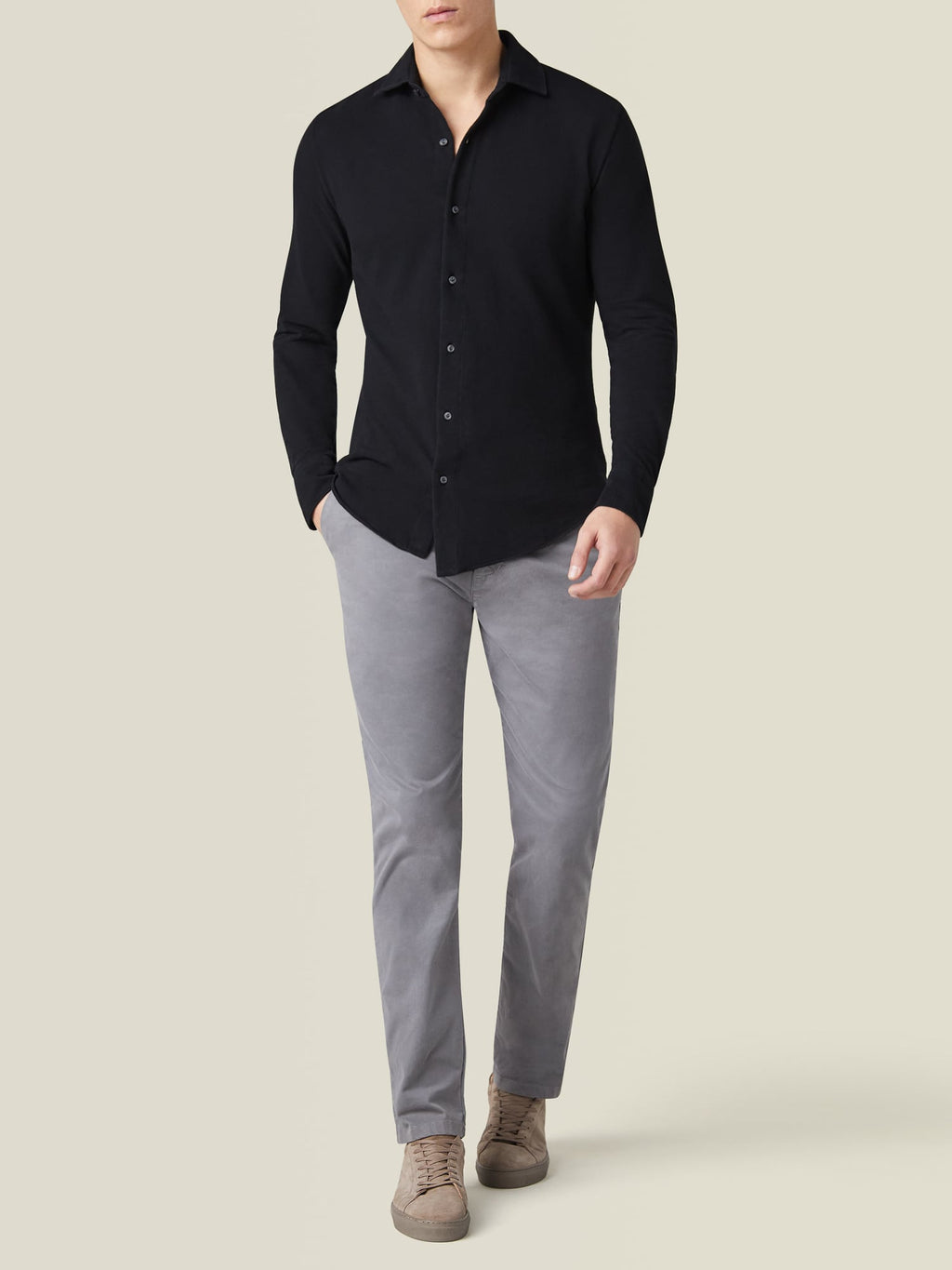 Full body shot of a model from the front wearing the black Siena Piqué Shirt with grey trousers and beige sneakers.