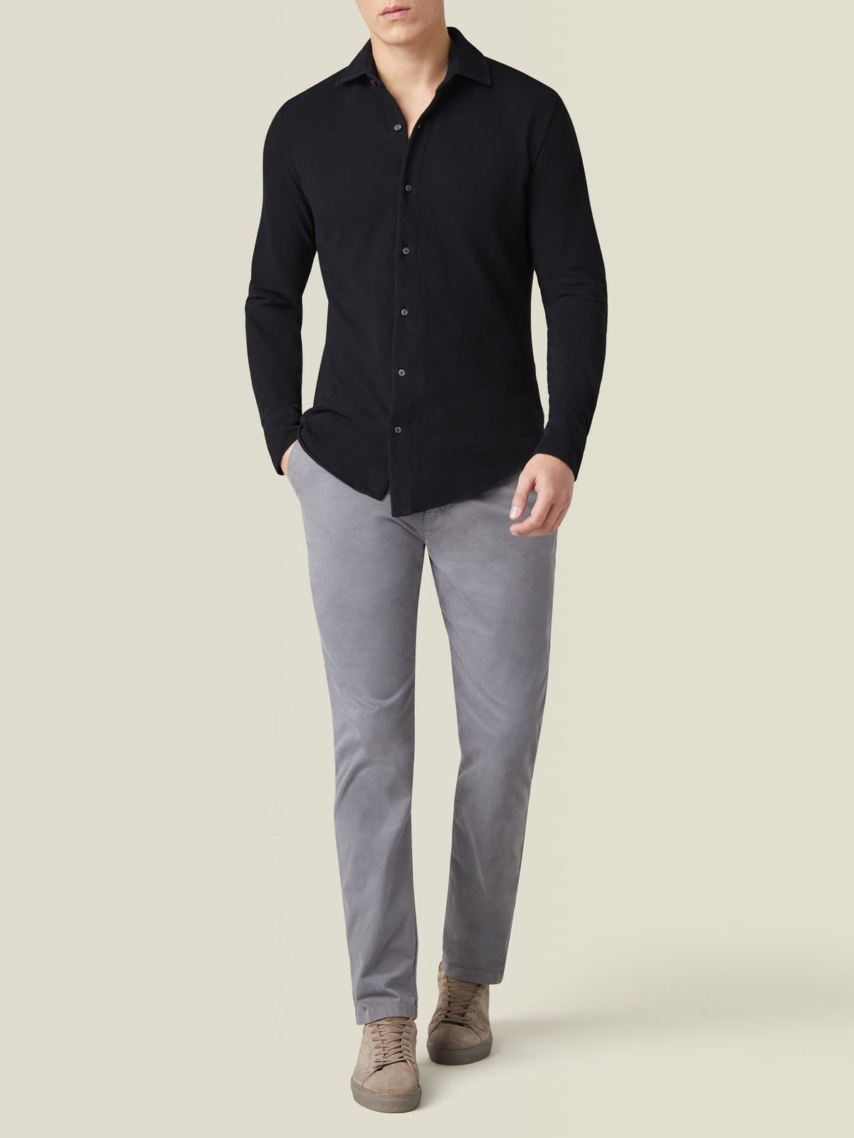Full body shot of a model from the front wearing the black Siena Piqué Shirt with grey trousers and beige sneakers.