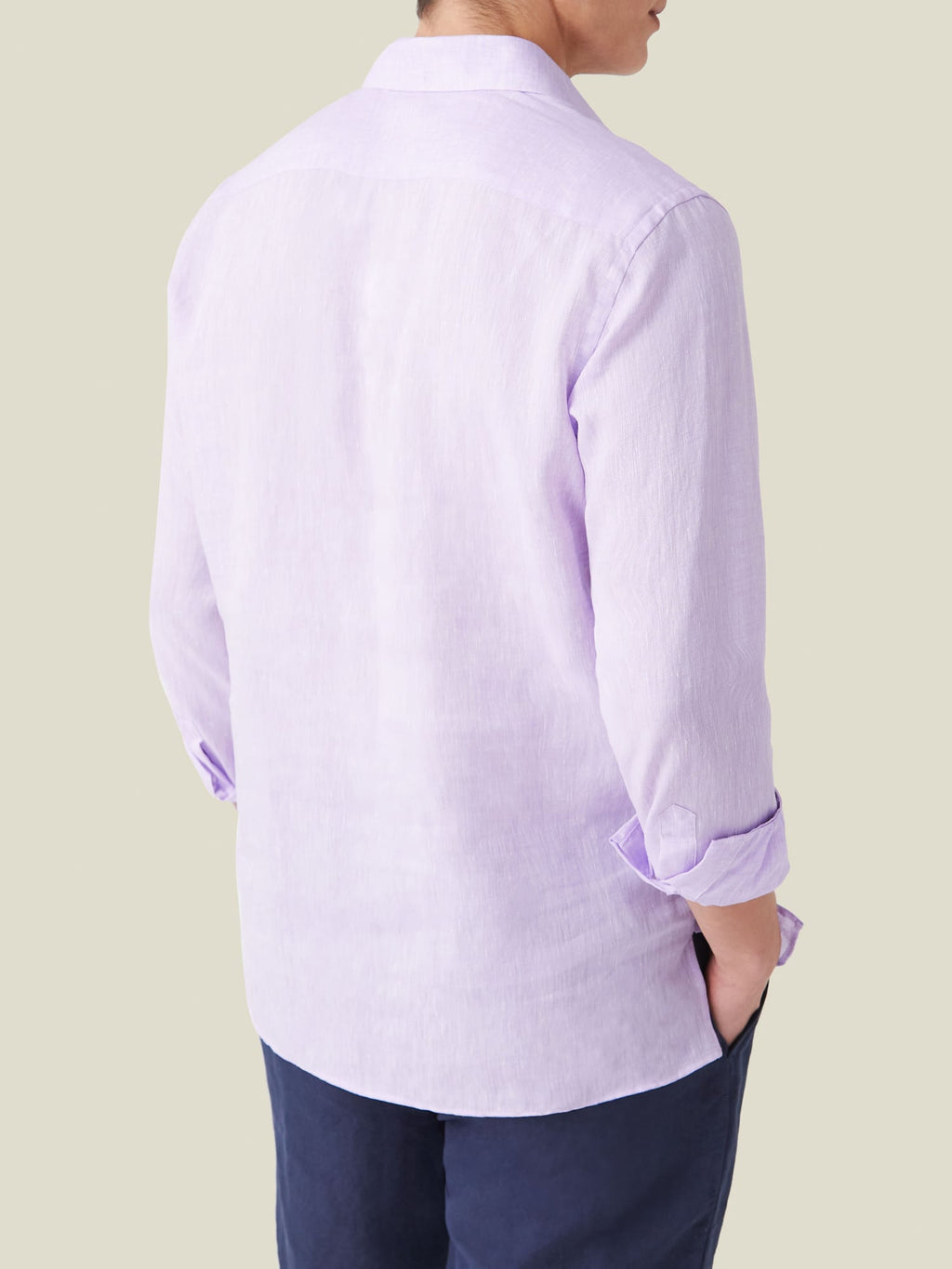 Man from behind wearing the lilac Ravello Linen Shirt with sleeves rolled up and hand in the pocket of his dark trousers.