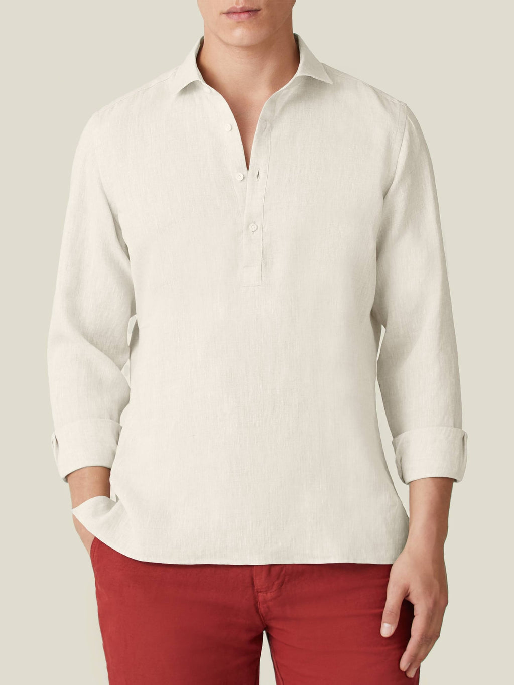 A model wears the Ravello Linen Shirt in Sand, shown from the front with sleeves rolled up and paired with red trousers.