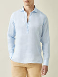 Model wears the Ravello Linen Shirt in sky blue, a long-sleeve popover style, shown from the front with tan trousers.