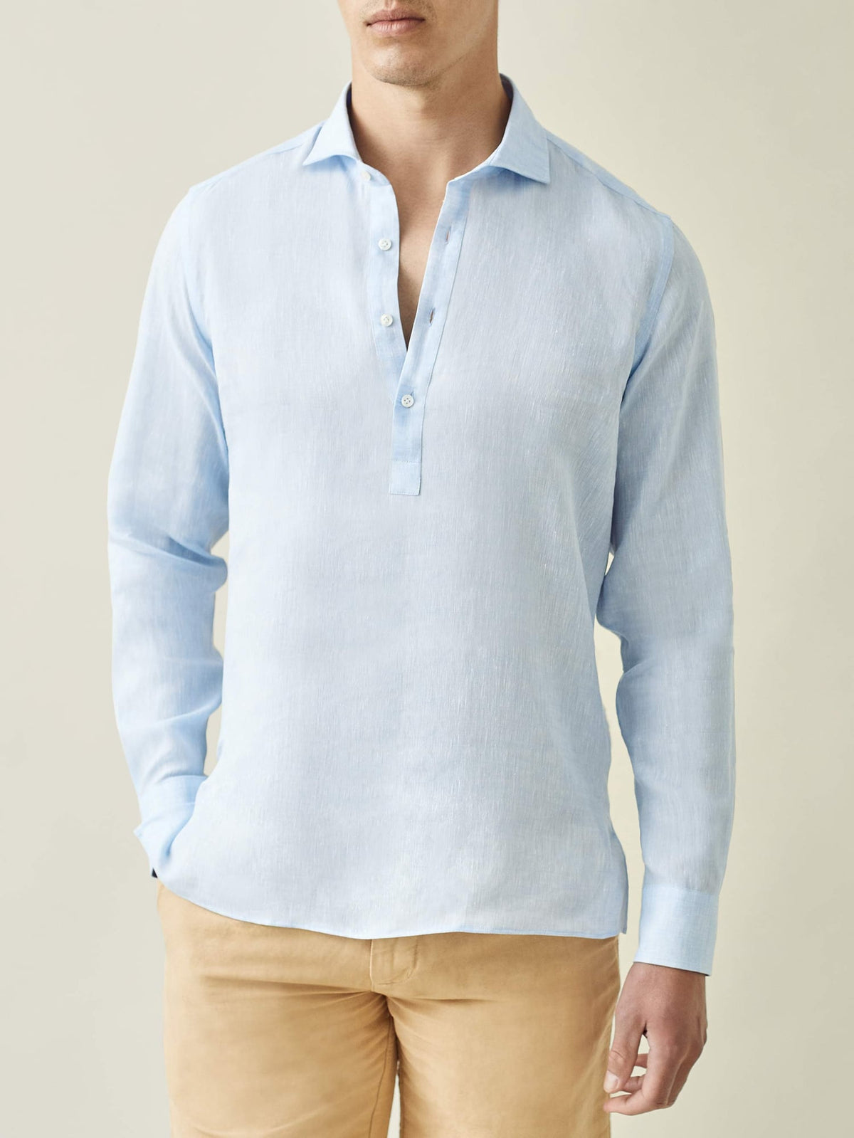 Model wears the Ravello Linen Shirt in sky blue, a long-sleeve popover style, shown from the front with tan trousers.