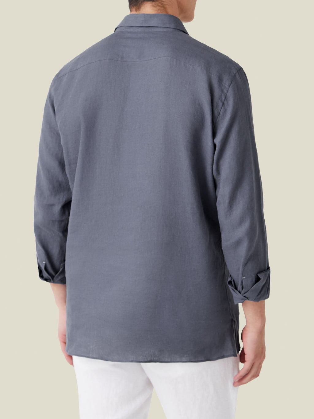 Back view of a man wearing the Payne's Grey Ravello Linen Shirt with rolled-up sleeves and white trousers.