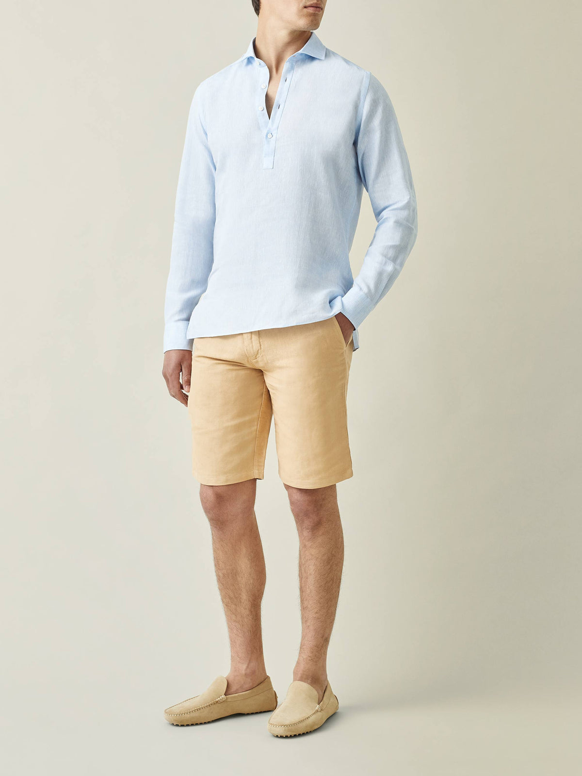 A man models the Ravello Linen Shirt in sky blue, paired with yellow shorts and cream loafers against a neutral background.