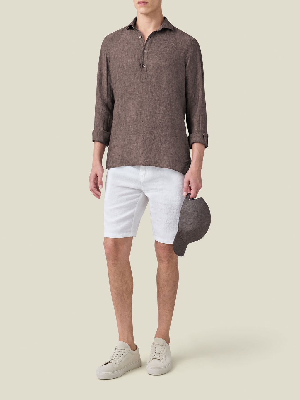Full-body shot of a model wearing the Ravello Linen Shirt in Chocolate Brown with white shorts and beige sneakers.