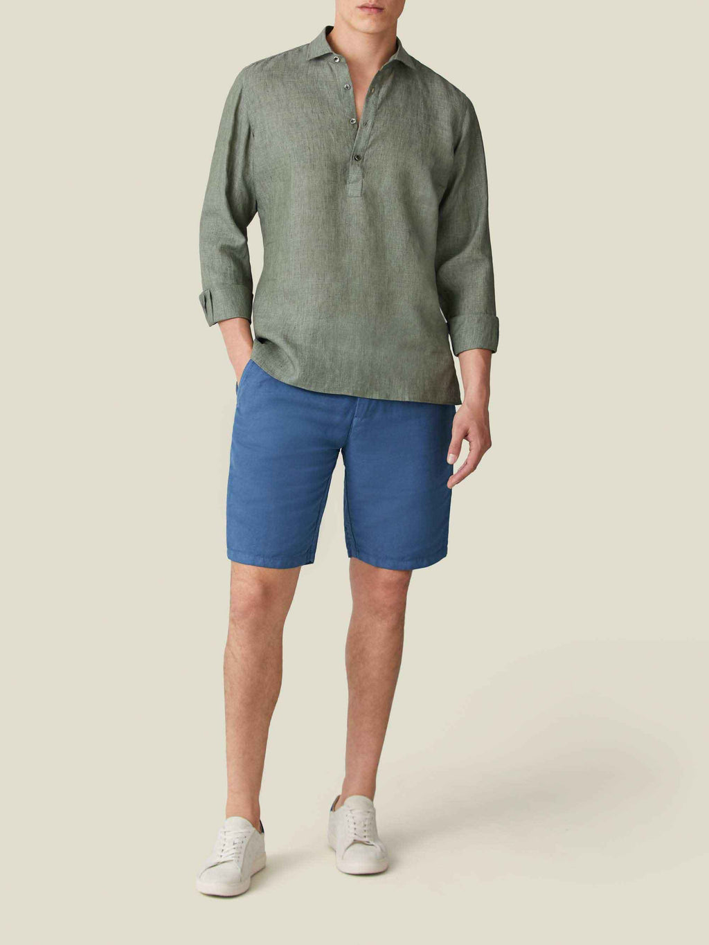 Front view of a model wearing the Ravello Linen Shirt in Safari Green, styled with blue shorts and white sneakers.