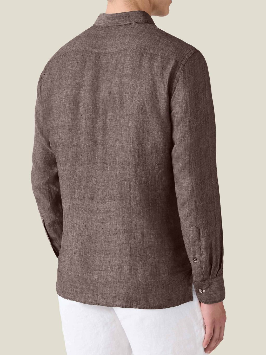 Back view of a model wearing the Ravello Linen Shirt in Chocolate Brown, paired with white trousers.