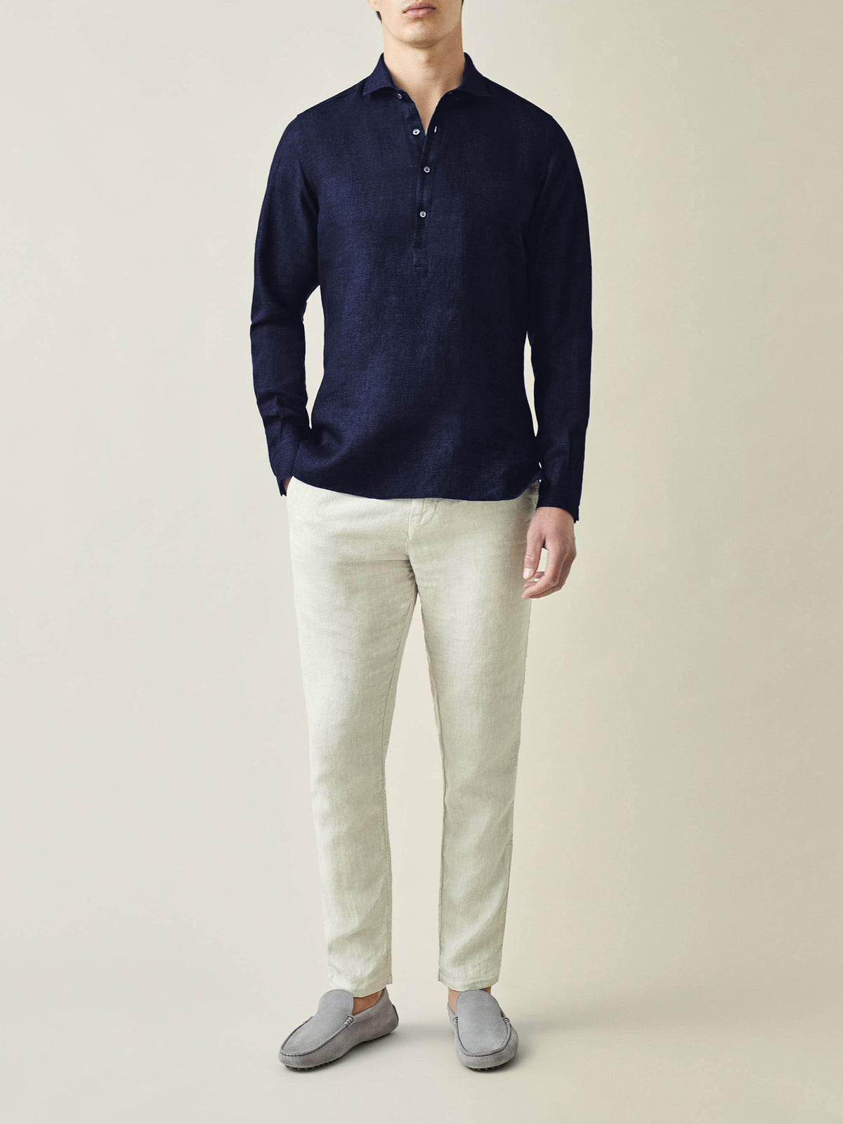 Model wears the Ravello Linen Shirt in Midnight Blue with cream trousers and grey loafers against a plain background.