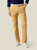 Model in Luca Faloni's mustard lightweight cotton chinos, styled with a navy shirt, woven belt, and white trainers.